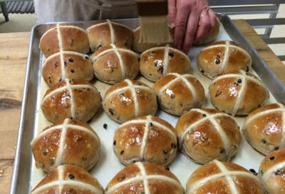 a pan of hot cross buns, hot from the oven, being brushed with syrup