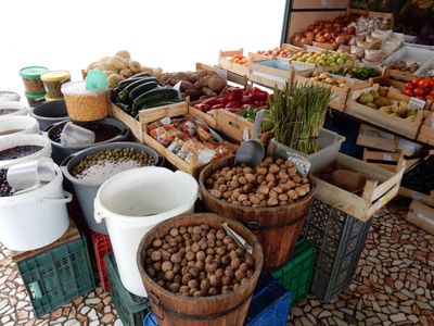a market stall; barrels of nuts and almonds, fresh produce, on a footpath made of broken pieces of pink marble.