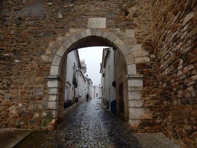 cobblestone footpath, passing under a stone arch, along a narrow side street.