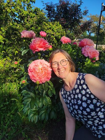 Cindy posing beside a pink peony flower, Beacon Hill Park. The bloom is nearly as big as her head too.